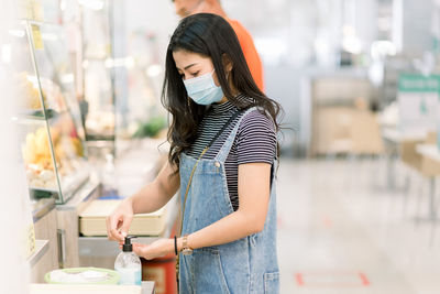 Woman wearing mask sanitizing hand at store