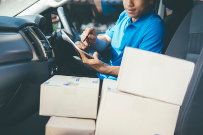 Midsection of delivery man with box sitting in car