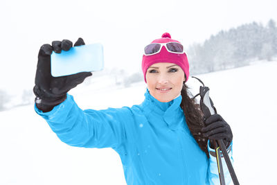 Woman taking selfie while standing on snow covered field