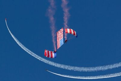 Low angle view of men paragliding with american flag in clear blue sky