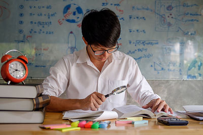 Young man studying with school supplies on table at home