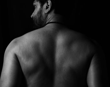 Rear view of shirtless man against black background