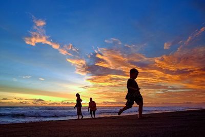 Silhouette children playing on beach against sky during sunset