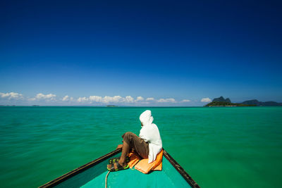 Rear view of man sitting on boat in sea against clear sky