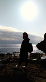 Rear view of silhouette man standing at beach against sky