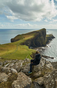 High angle view of woman sitting on cliff by sea 