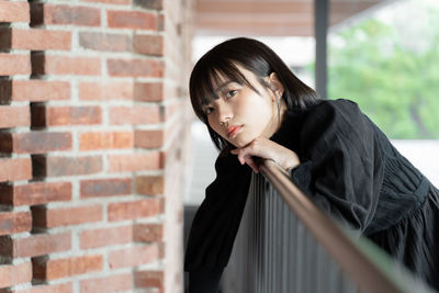 Young woman looking away against brick wall