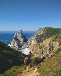 Rear view of people walking on shore against clear blue sky