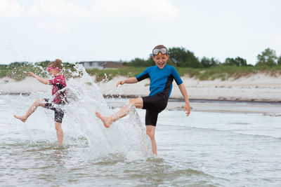 Girl with brother splashing water at beach