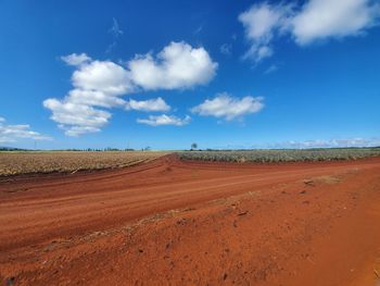 Dirt road on field against sky