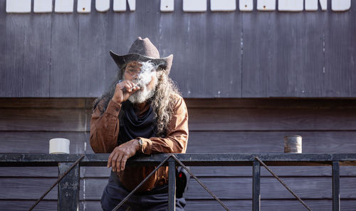 A tobacco pipe is smoked by a cowboy wearing a wide-brimmed hat and a headband.