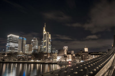 Illuminated buildings by river against sky at night