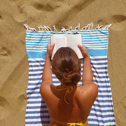 Rear view of woman on sand at beach reading 