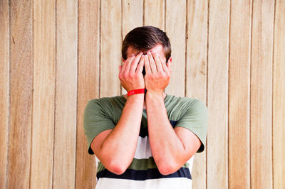 Young man covering face against fence