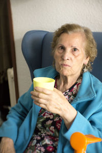 Portrait of senior woman holding drink while sitting at home