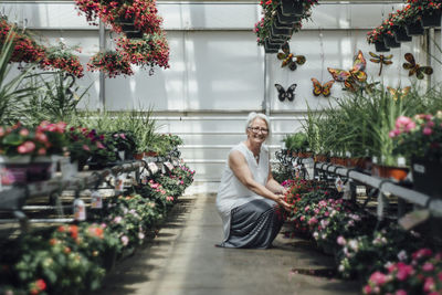 Portrait of mature woman crouching by plants at greenhouse