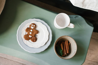 Gingerbread man cookies on a white plate, cinnamon sticks and a mug on a green table