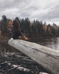 Woman sitting on log in forest against sky