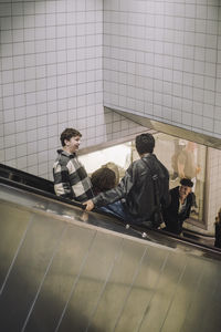 Happy male and female teenage friends moving down from escalator at mall