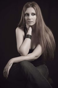 Portrait of young woman sitting against black background