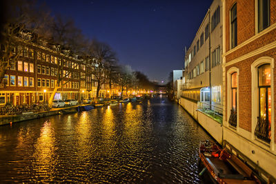 Canal amidst illuminated buildings in city at night