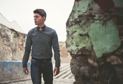 Young man looking away while standing by rock