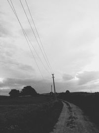 Electricity pylon on road amidst field against sky