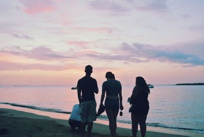 Rear view of friends on beach against sky during sunset