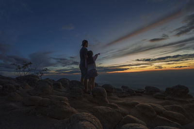 Man standing on rock against sky during sunset