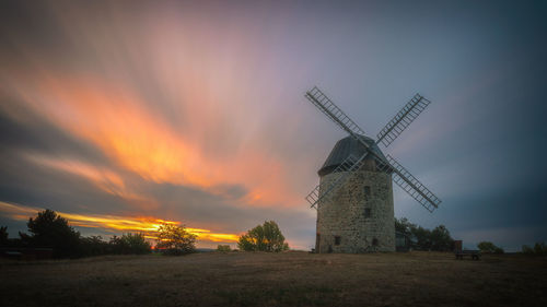 Traditional windmill on field against sky during sunset