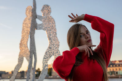 Portrait of young woman gesturing while standing against statue in city