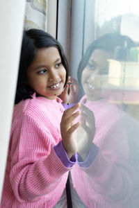 A cute indian girl child standing and looking through glass window with reflection