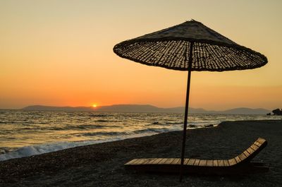 Lounge chair below parasol at beach during sunset