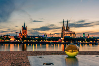 Illuminated buildings by river during sunset