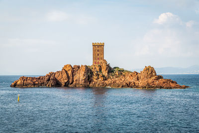 Built structure on rock by sea against sky