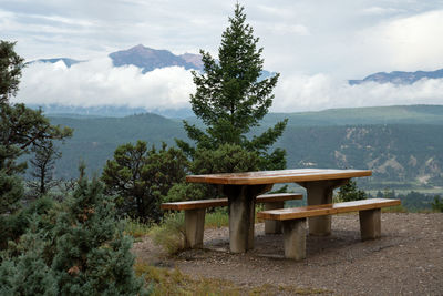 Bench and tables against trees and mountains against sky