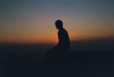 Silhouette man sitting against orange sky during sunset