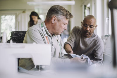 Mature fashion designer showing fabric to male colleague at workshop