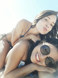 Low angle portrait of female friends relaxing against sky at beach