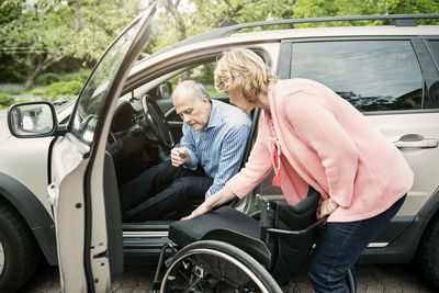 Woman assisting disabled man in disembarking from car