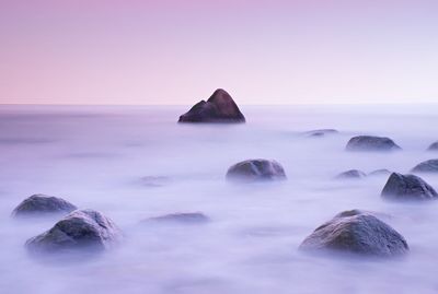 Rocks in sea against sky during sunset