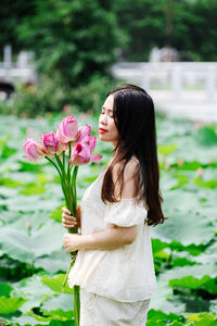 Portrait of young woman standing by flowering plants