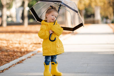 Full length of cute girl with umbrella standing on road