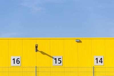 Low angle view of numbers on yellow wall against sky during sunny day