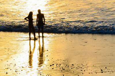 People standing on beach against sky during sunset