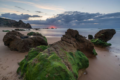 Rocks on beach against sky during sunset