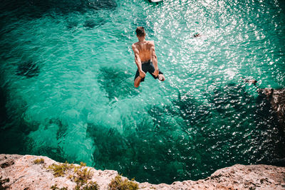 Full length of shirtless man jumping in the sea