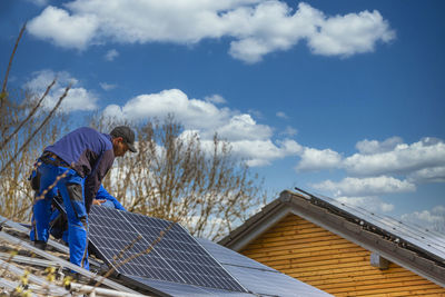 Man working on roof of house against sky