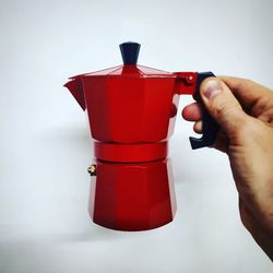 Close-up of hand holding red drink against white background