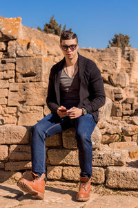 Full length of man sitting on stone wall